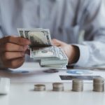 Manos de cajeros bancarios contando billetes en dólares sobre la mesa, concepto financiero y de inversión.