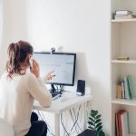 Work from home during coromavirus pandemic. Woman stays home talking on phone. Workspace of freelancer. Office interior with computer